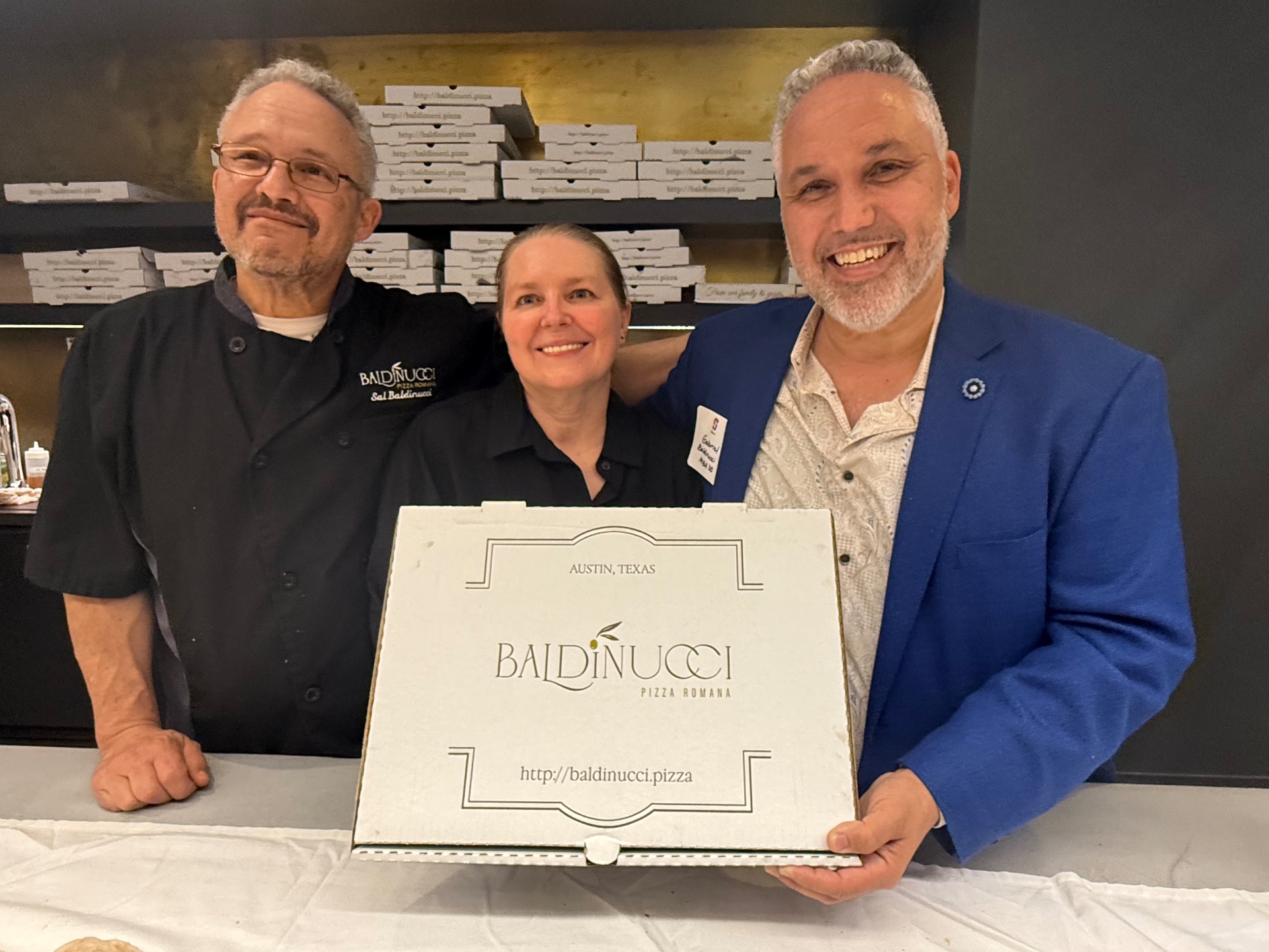 Baldinucci Pizza team in the kitchen holding a pizza box
